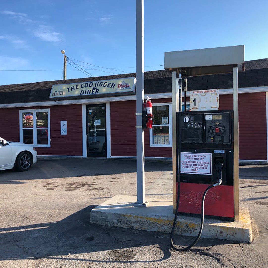 Photo of the Cod Jigger Diner. There's a single gas pump in the parking lot. The sign over the door has the Cod Jigger logo flanked by a Coors light logo and a Molson Canadian logo.